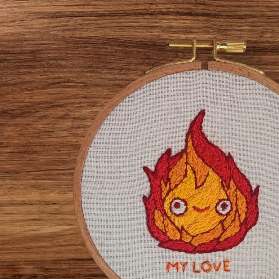 Décoration brodée à la main représentant Calcifer, personnage du Château ambulant de Ghibli, dans un tambour à broder en bois