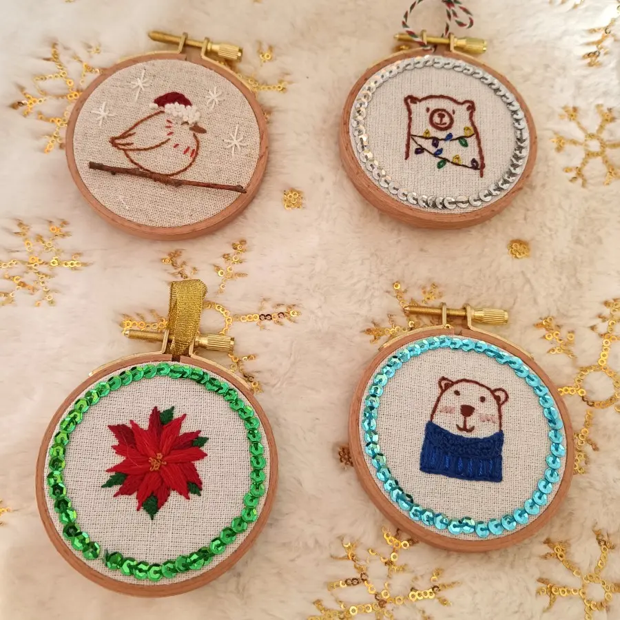 Boules de Noël brodées à la main représentant des motifs d’hiver, montées sur tambour à broder en bois.