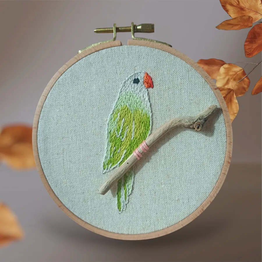 Broderie d'une petite perruche verte sur un vrai morceau de bois artisanale