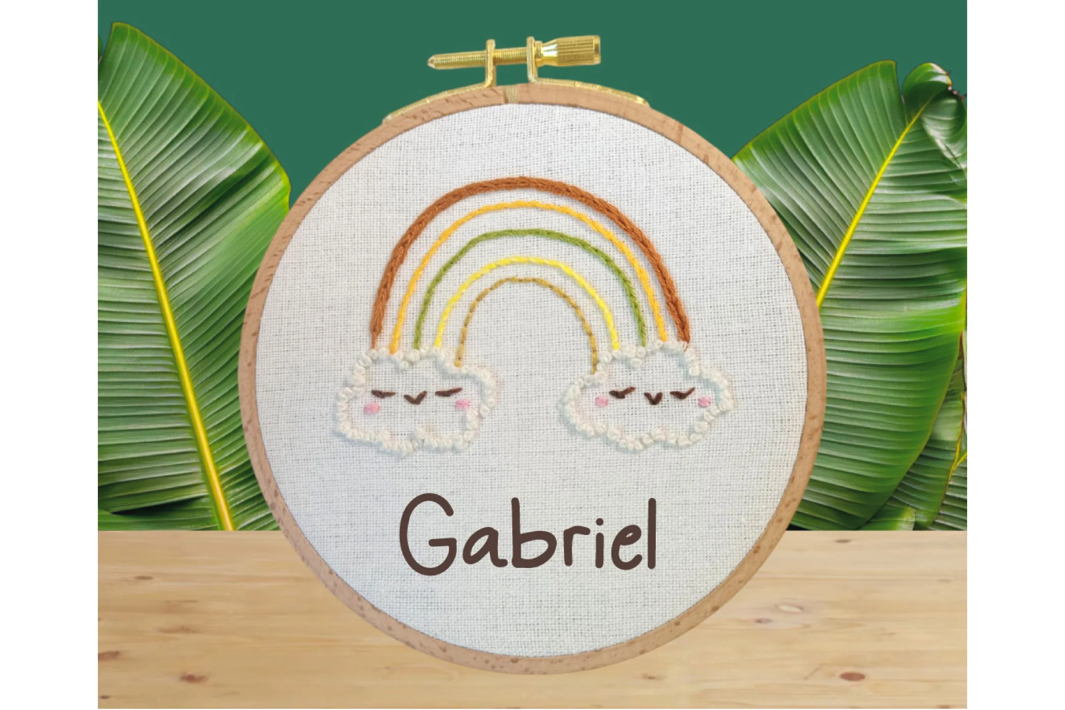 Broderie d'un arc en ciel avec un nuage souriant à chaque bout, le prénom gabriel ajouté numeriquement pour simuler un bat