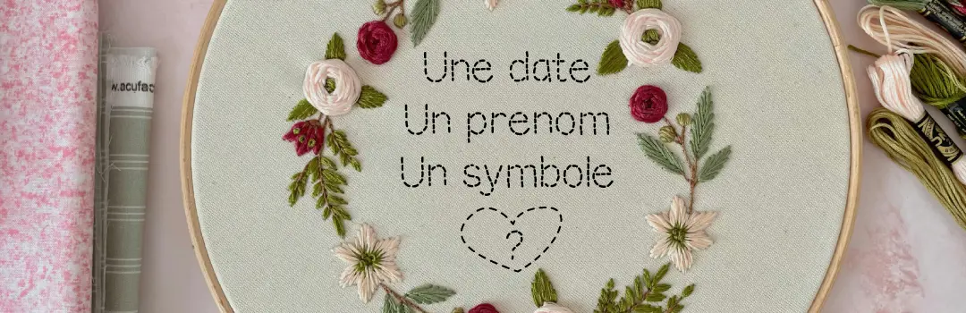 Toile broderie d'un rond florale et à l'interieur le texte 'une date un prenom un symbole' avec un coeur et un point d'interrogation